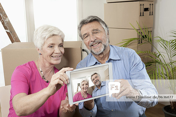 Senior couple taking photographs on digital phone in new apartment