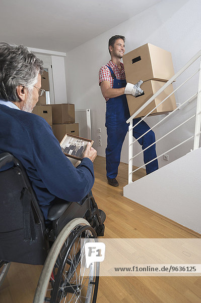 Handicapped old man looking at photograph and removal man carrying cardboard box upstairs
