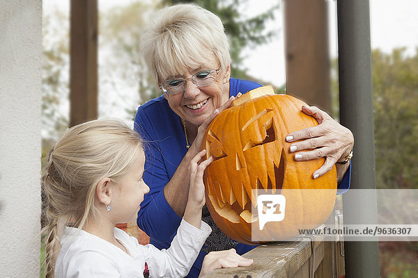 Senior woman showing Halloween pumpkin to her granddaughter