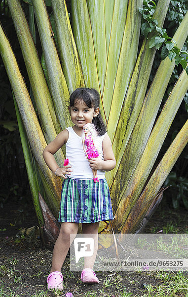Mädchen  4 Jahre  mit Barbiepuppe  posiert vor einer Palme  San Juan de Nicaragua oder San Juan del Norte oder Greytown  Rio San Juan  Nicaragua  Nordamerika