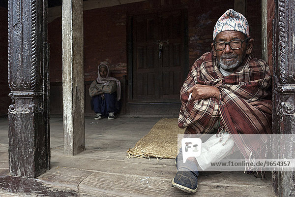 Nepalese  eingehüllt in eine Decke sitzt an einem Eingang  Bhaktapur  Nepal  Asien