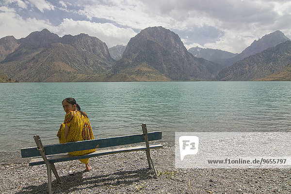 Woman sitting on a bench at the turquoise Alexander lake in the Fan Mountains  Iskanderkul  Tajikistan  Central Asia  Asia