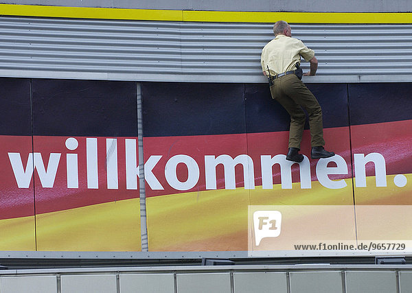 'Sonderparteitag und Wahlkampfauftakt der CDU in der Westfalenhalle Dortmund  Ein Polizist klettert an der Mauer eines Vordaches der Westfalenhalle hoch  die mit Deutschlandfahne und dem Wort ''Willkommen.'' geschmueckt ist.'