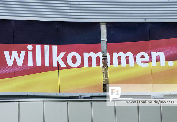 'Sonderparteitag und Wahlkampfauftakt der CDU in der Westfalenhalle Dortmund  Ein Polizist schaut pruefend durch die Luecke einer Tafel die mit Deutschlandfahne und dem Wort ''Willkommen.'' geschmueckt ist.'