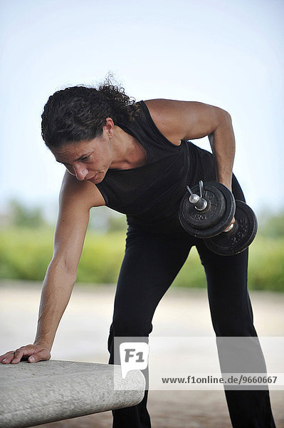 Eine Frau trainiert mit Gewichten in einem Park