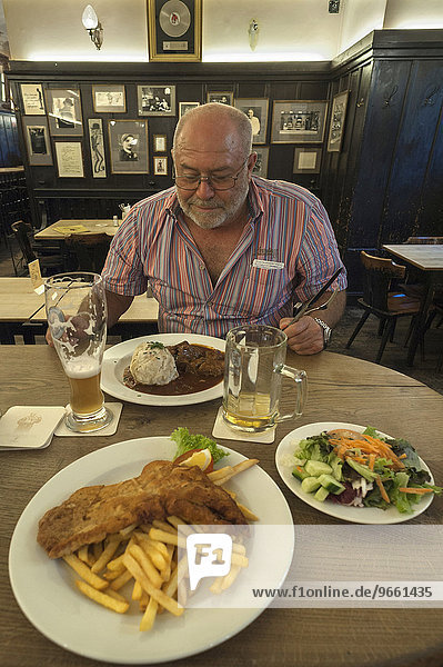 Elderly man sitting in front of a hearty meal  at the front a plate of schnitzel and chips in a Bavarian restaurant  Munich  Upper Bavaria  Bavaria  Germany  Europe