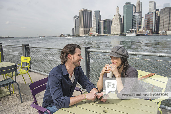 Happy couple sitting and using tablet pc and drinking coffee with cityscape in background