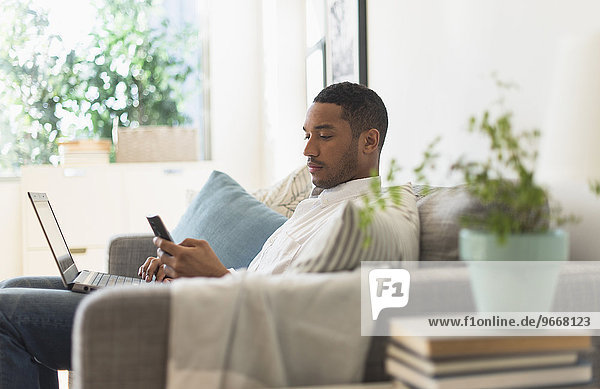 Man sitting in living room  using laptop and cell phone