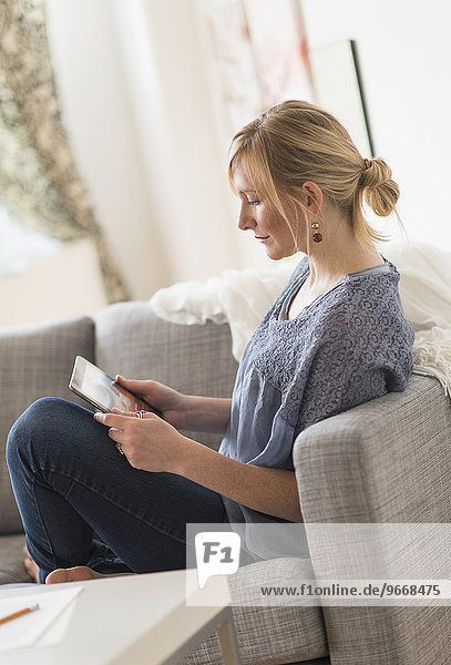 Pensive woman sitting on sofa with tablet pc