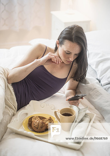 Woman having breakfast in bed  using mobile phone