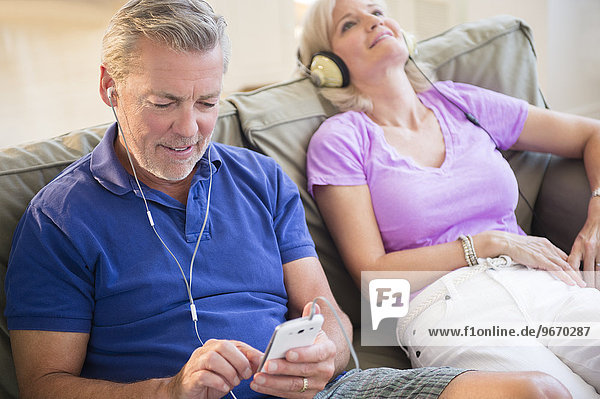 Portrait of couple sitting on sofa listening to music on headphones