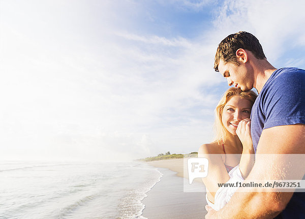 Portrait of young couple embracing on sandy beach  against background of coastline