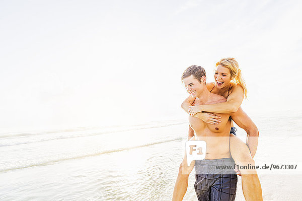 Boyfriend carrying girlfriend piggyback on beach