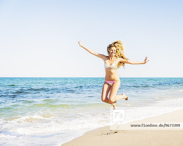 Portrait of young woman wearing bikini jumping on beach