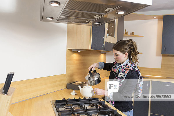Woman pouring water at teapot in kitchen