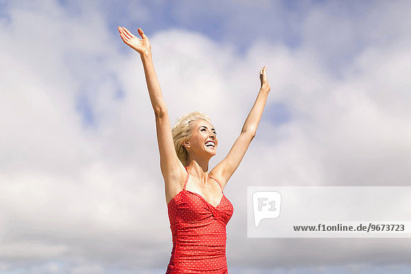 Woman wearing red one piece swimsuit rising arms and smiling