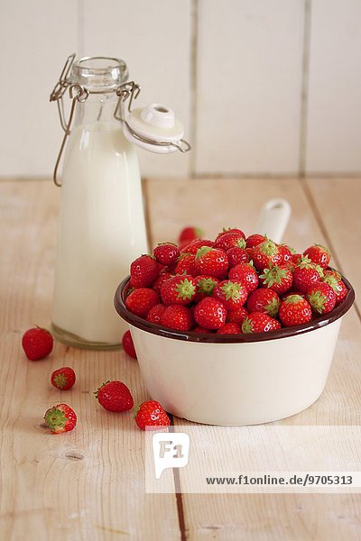 Erdbeeren im Stieltopf neben einer Milchflasche