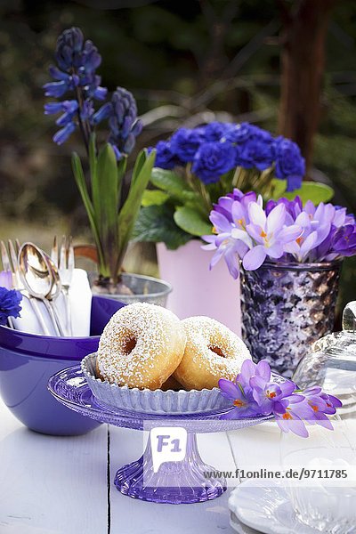 Donuts auf Tisch im Freien dekoriert mit Geschirr & Blumen in Lila-& Blautönen