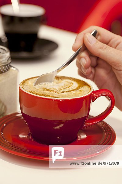Hand rührt in heissem Cappuccino mit Herzdekoration