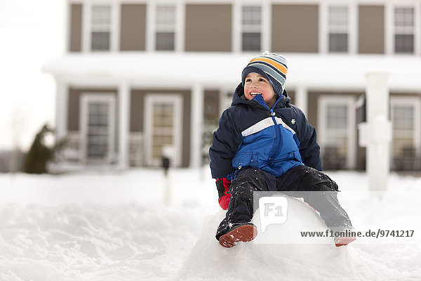 Mixed race boy sitting on large snowball