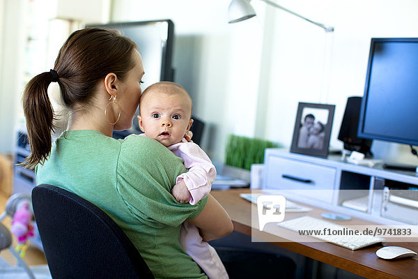 Caucasian mother working in home office and holding baby
