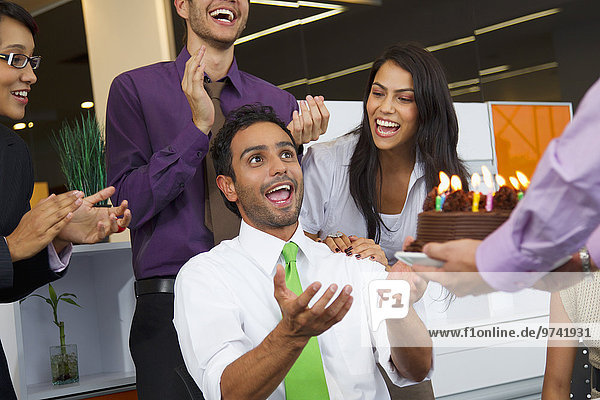 Hispanic co-workers surprising businessman with birthday cake