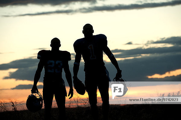 Silhouette of Black football players carrying helmet and football