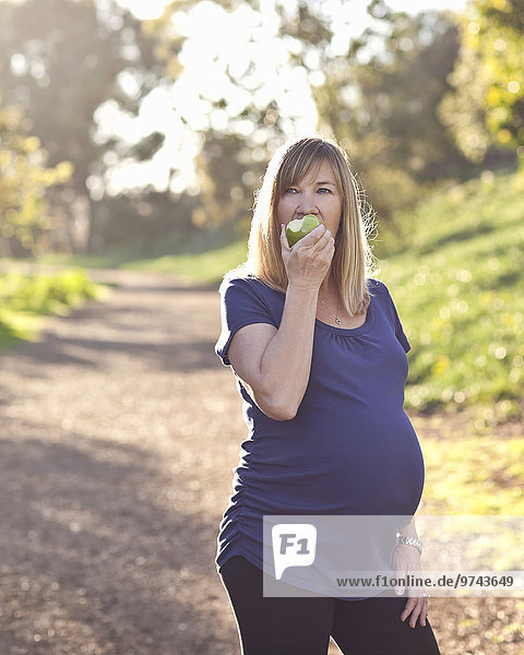 Pregnant Caucasian woman eating apple outdoors