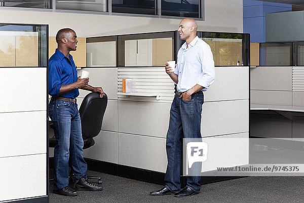 Mixed race businessmen talking in modern office cubicle