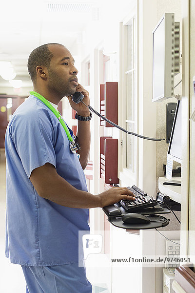 Black doctor using equipment and talking on telephone in hospital