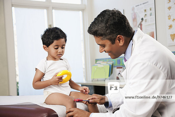 Indian doctor testing boy's reflexes in doctor's office