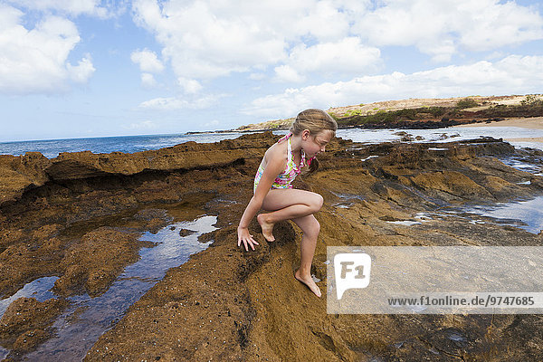 Caucasian girl playing on rocks near ocean