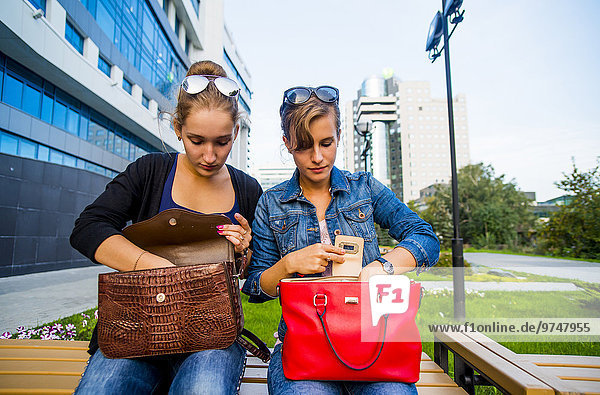Caucasian women searching in purses on park bench