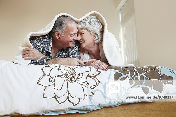 Older couple rubbing noses under blanket on bed