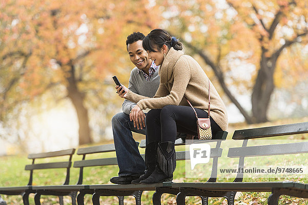 Couple using cell phone on park bench