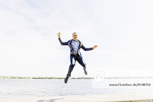 Black businessman jumping for joy at waterfront