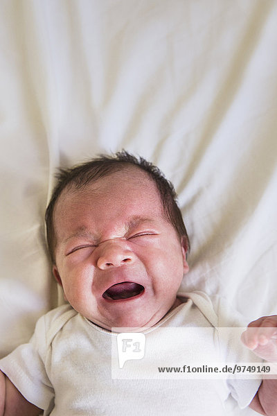 Close up of mixed race baby crying on bed
