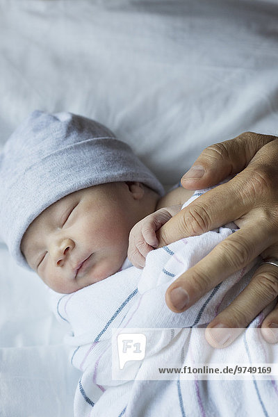 Close up of newborn baby holding finger of father