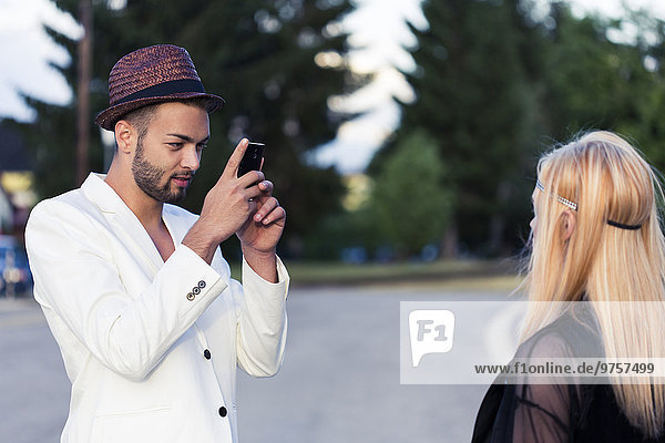 Stylish young man taking a photo of his girlfriend with smartphone