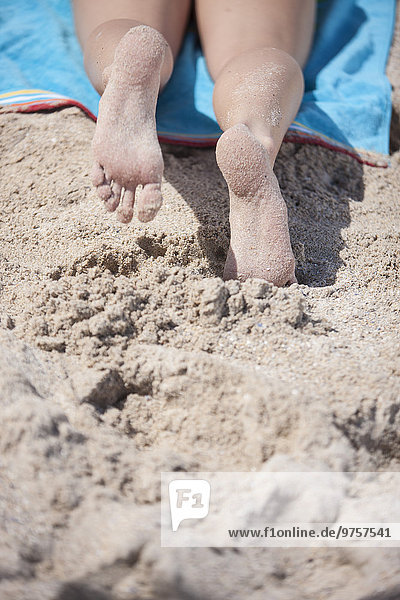 Beine einer jungen Frau am Strand liegend