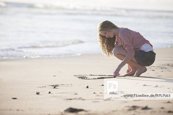 Young woman drawing heart in sand on the beach