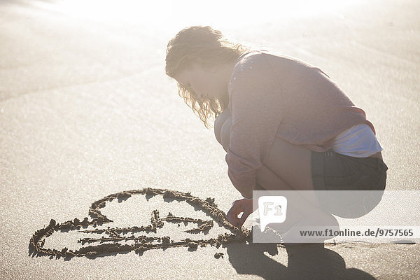Young woman drawing heart in sand on the beach