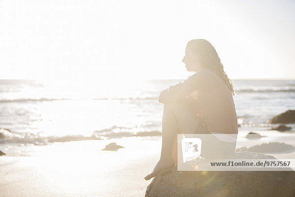 Young woman sitting on rock on the beach at sunset