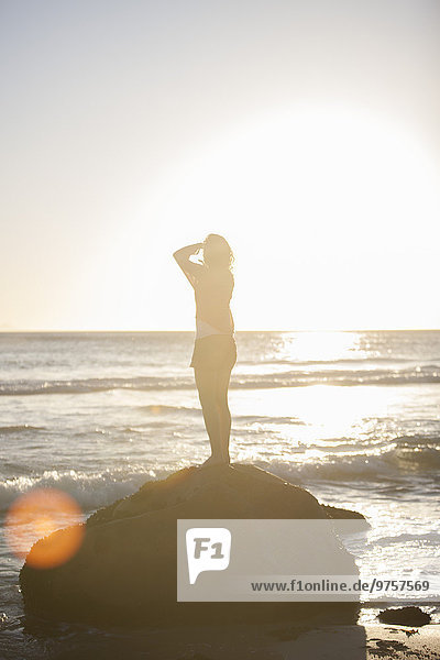 Young woman standing on rock on the beach at sunset