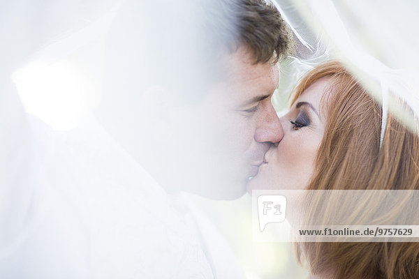 Bräutigam und Braut küssen sich unter dem Schleier