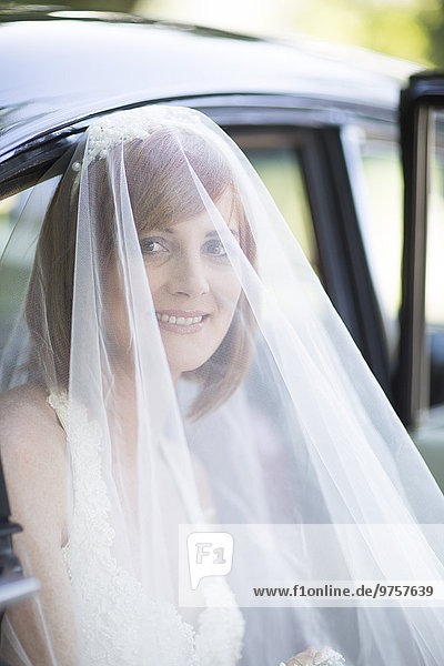 Lächelnde Braut  die vor ihrer Hochzeit aus dem Auto steigt.