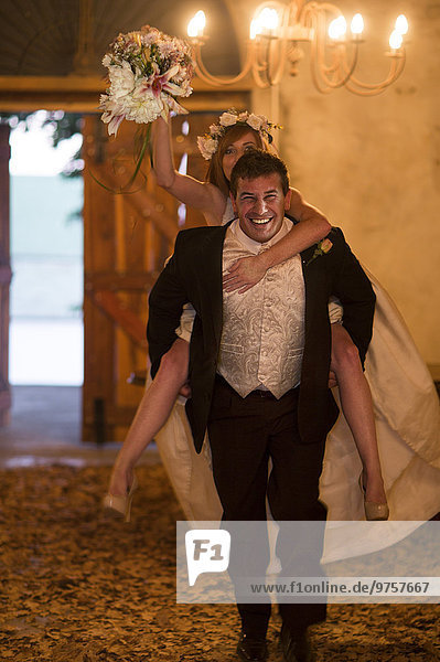 Fröhlicher Bräutigam mit Braut-Huckepack in der Lobby