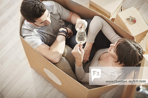 Couple moving house sitting in a box and clinking wine glasses