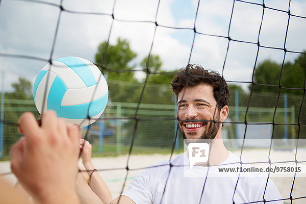 Lächelnder junger Mann am Netz des Beachvolleyballfeldes