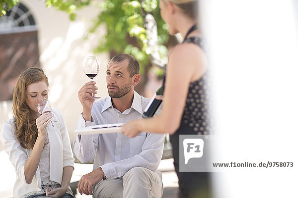 Waitress with tray and couple sitting outdoors tasting red wine